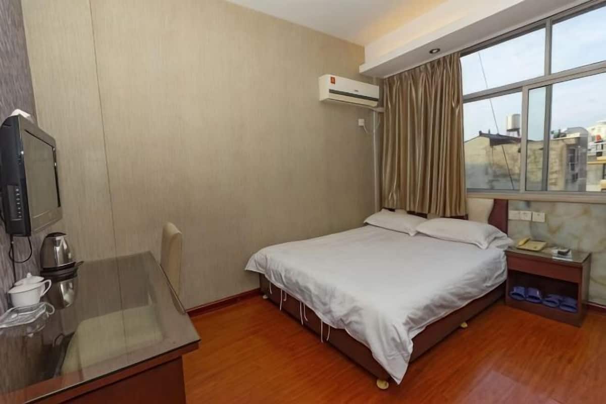 A hotel room with a bed, a desk with a computer, a TV, and a window with curtains.