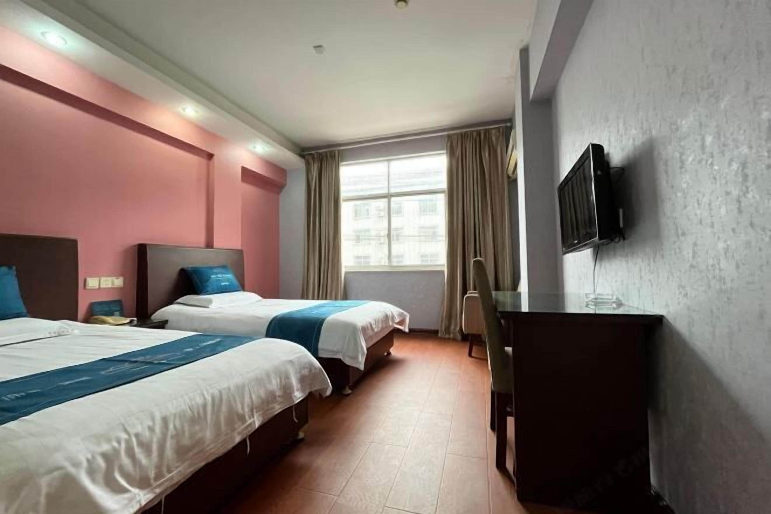 A hotel room with two beds, a desk, a TV, and a window with curtains.