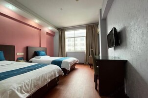 A hotel room with two beds, a desk, a TV, and a window with curtains.