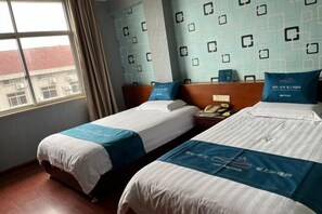 Habitación de hotel con dos camas, una ventana y papel tapiz estampado.