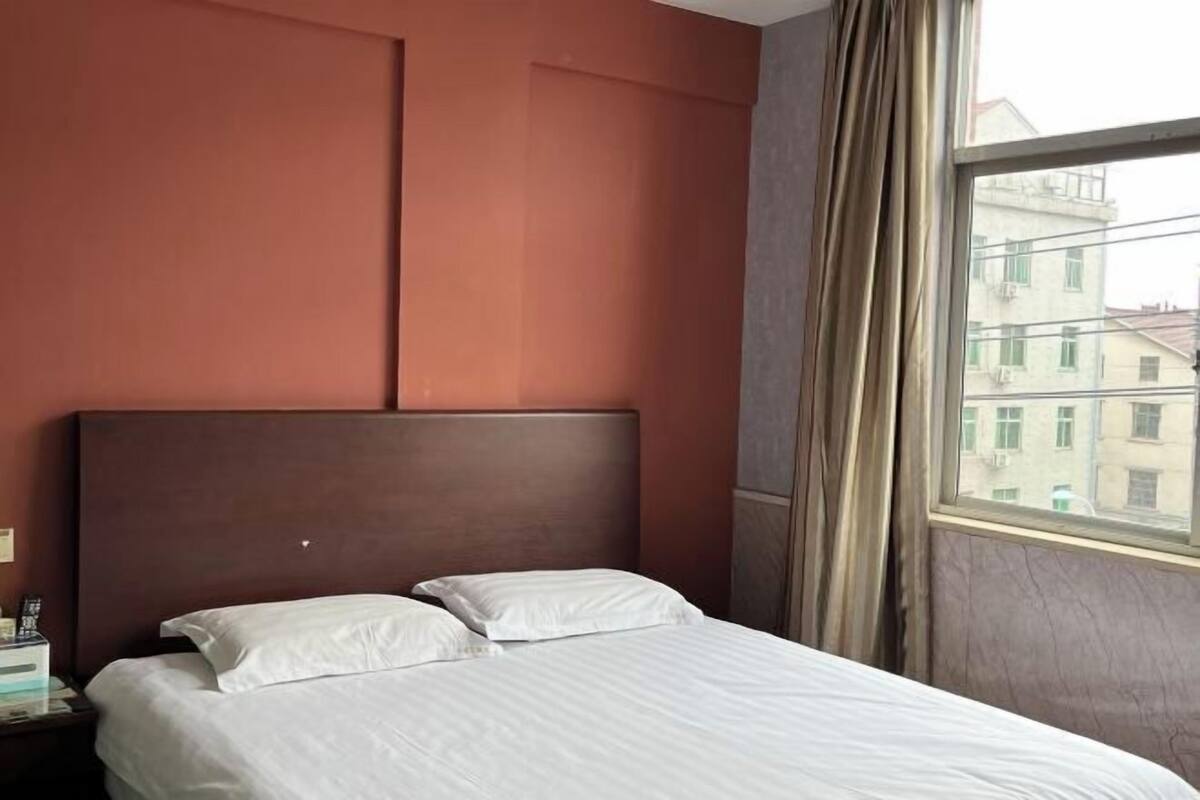 A hotel room with a bed, a nightstand, and a window with curtains.