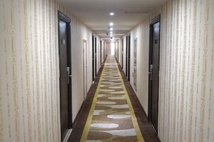 A hotel corridor with doors on both sides, a patterned carpet, and a ceiling light.