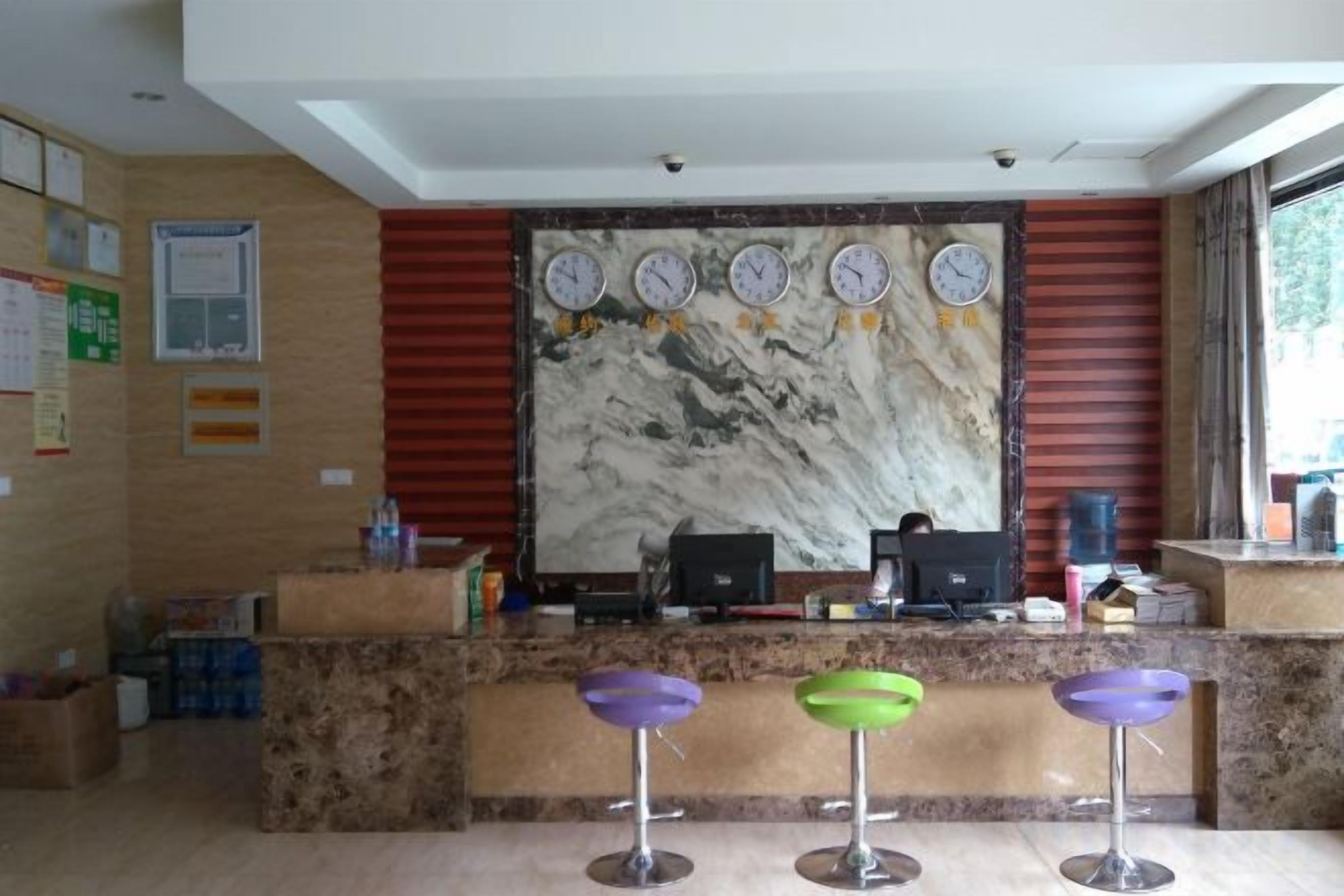 Una zona de recepción con pared de mármol, relojes, un mostrador y tres taburetes de bar.