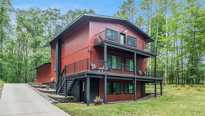A two-story red house with a balcony, surrounded by trees. - Big Red! Modern clubhouse with Hot Tub! Walking distance to Castle - 4 bedrooms (Stanwood)