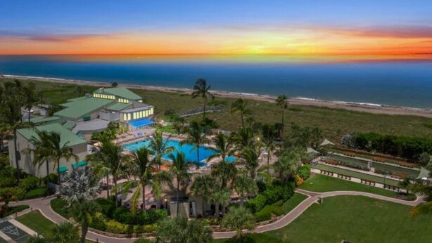Un resort con piscina, palme e vista sull'oceano al tramonto.
