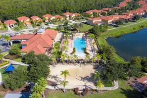 An aerial view of a resort with a central swimming pool, multiple buildings with red roofs, and a surrounding landscaped area with palm trees. - Family-Friendly 3BR Home w/ Pool, BBQ & Themed Rooms – 15 Min to Disney! (Kissimmee)