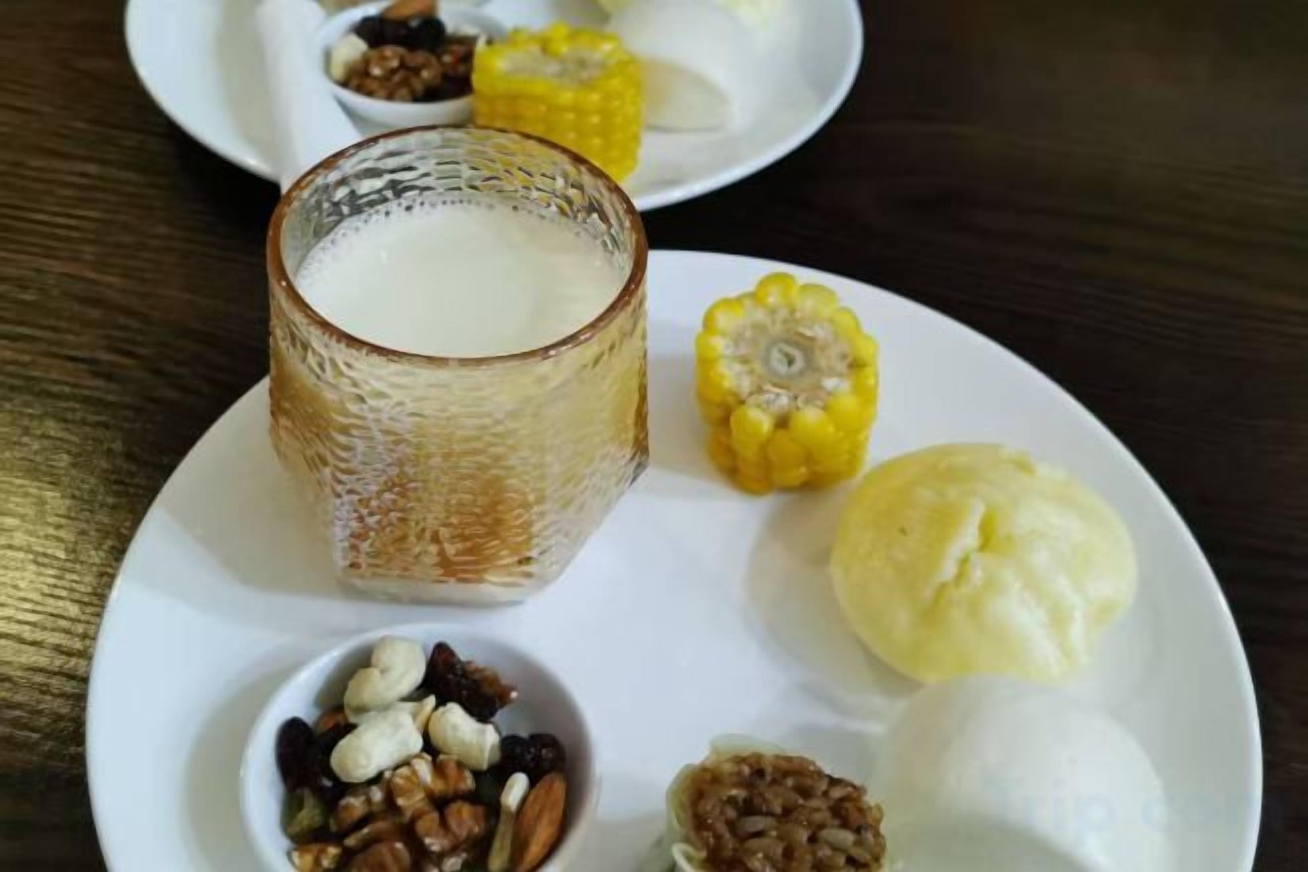 Een bord met een glas melk, een kolf mais, een bol ijs en een schaal vol noten.