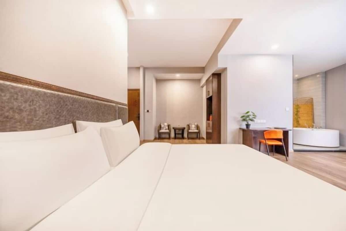 Habitación de hotel con una cama grande, un escritorio con silla, una mesita y un baño con bañera.