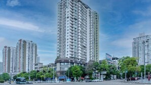 A high-rise building with a curved facade, surrounded by other tall buildings and a busy street with vehicles and traffic lights. - Manfu Hotel (Beibei Southwest University Zhuangyuanbei Subway Station Branch) (Chongqing)