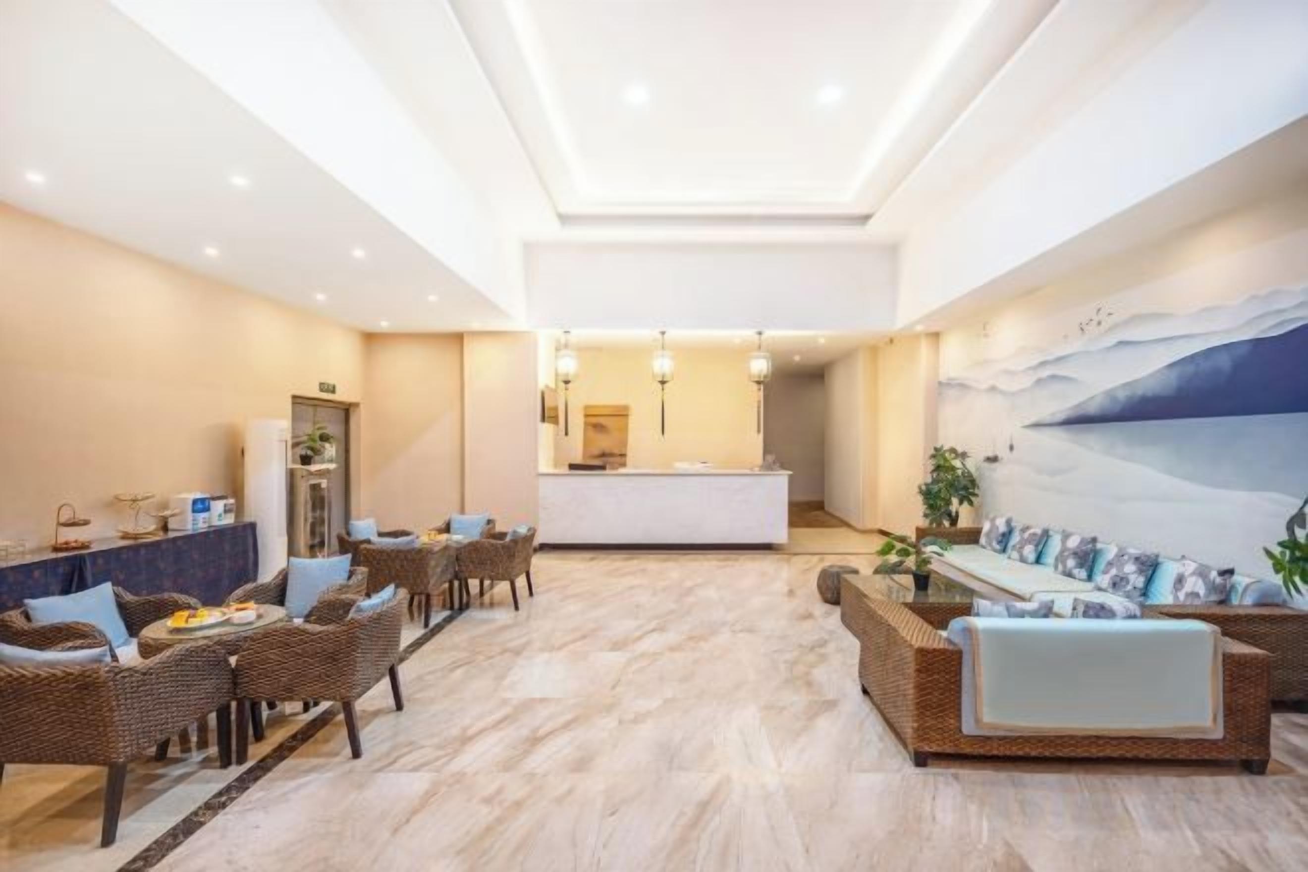 Un vestíbulo amplio con una mesa de recepción, muebles de mimbre y un mural grande en la pared.