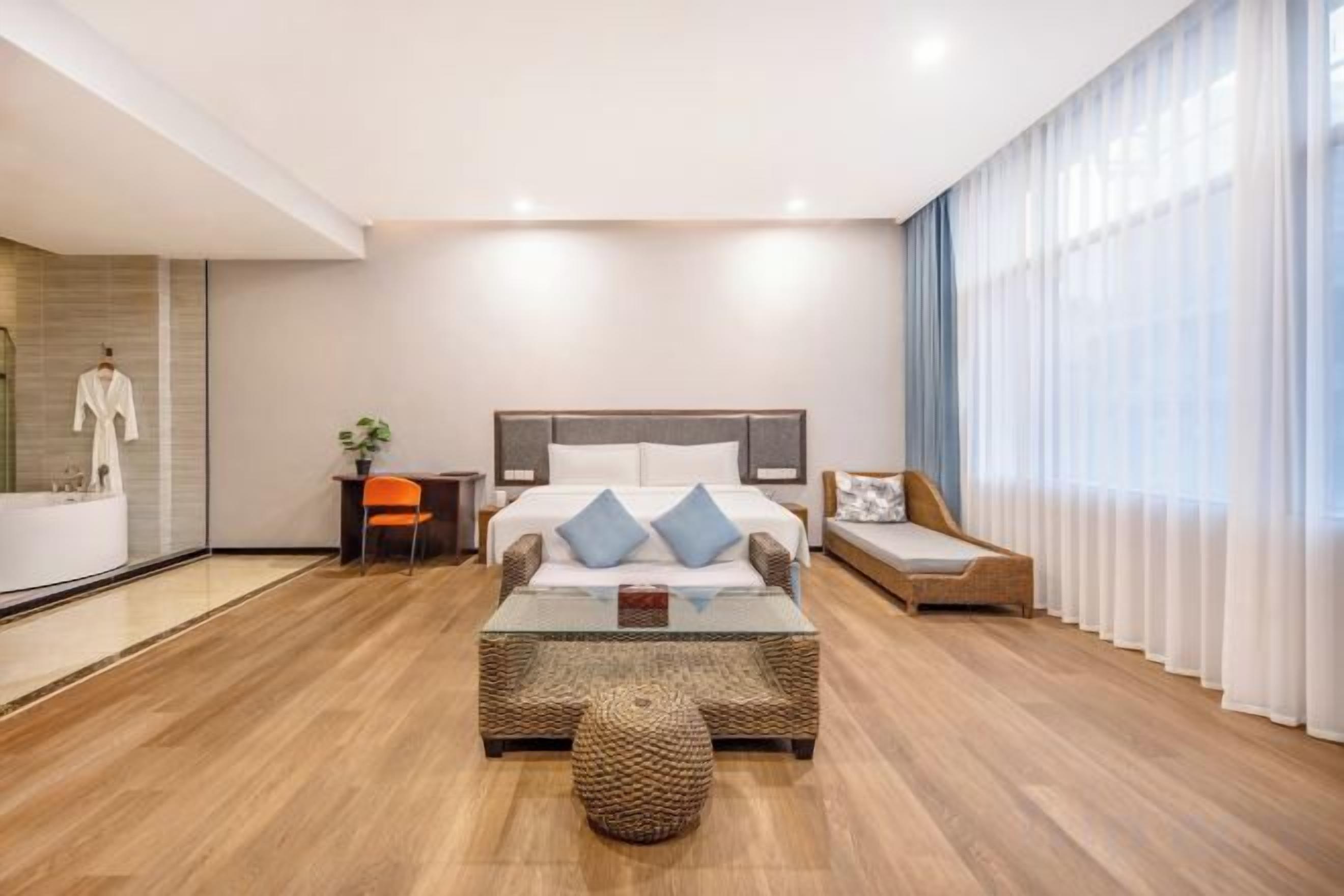 Una habitación de hotel moderna con una cama grande, una mesa de centro de cristal y una zona de estar con sofá.