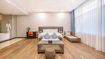 Una habitación de hotel moderna con una cama grande, una mesa de centro de cristal y una zona de estar con sofá.