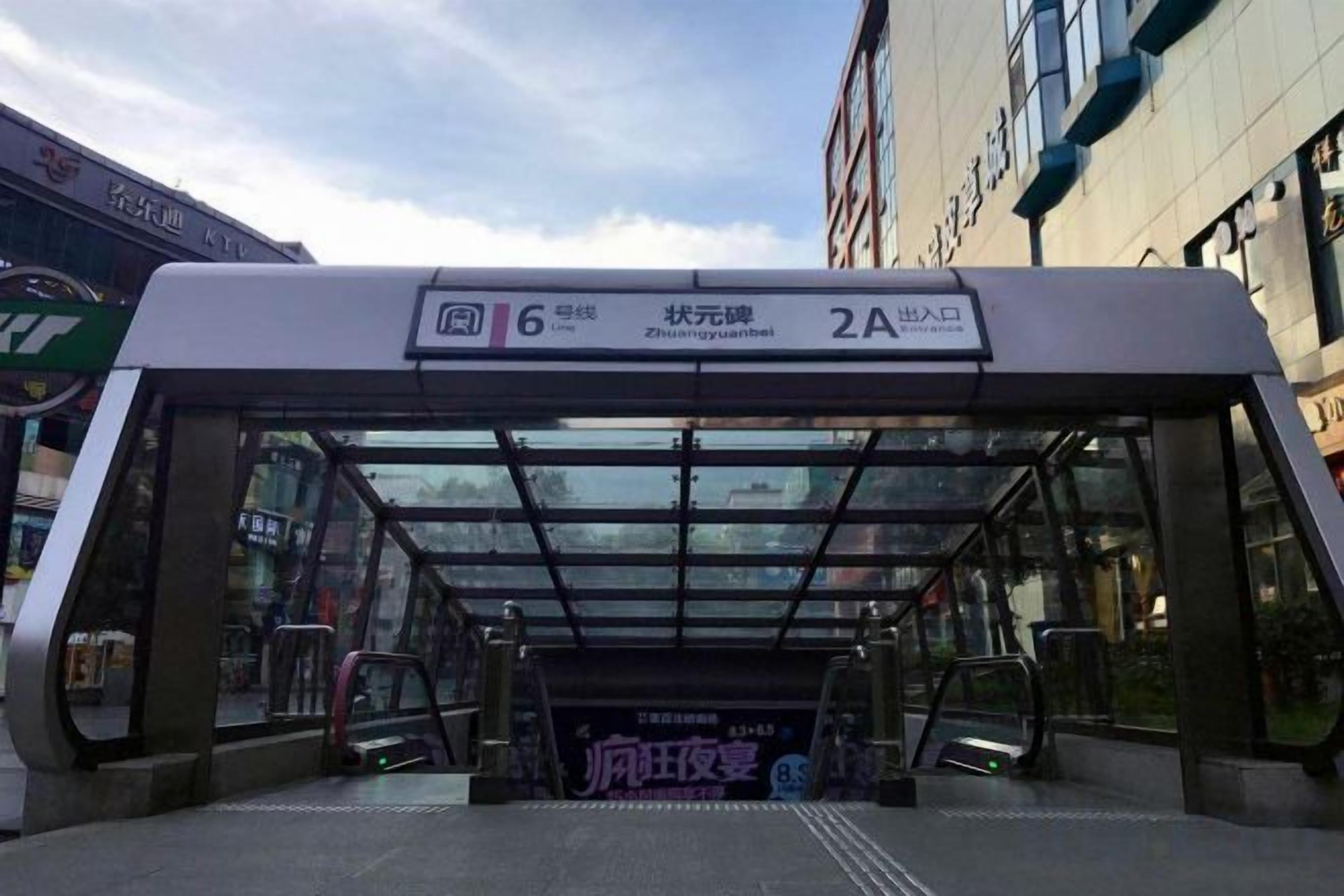 Un refugio de autobús con techo transparente, un cartel que indica la ruta 6 de autobús y una pantalla digital.