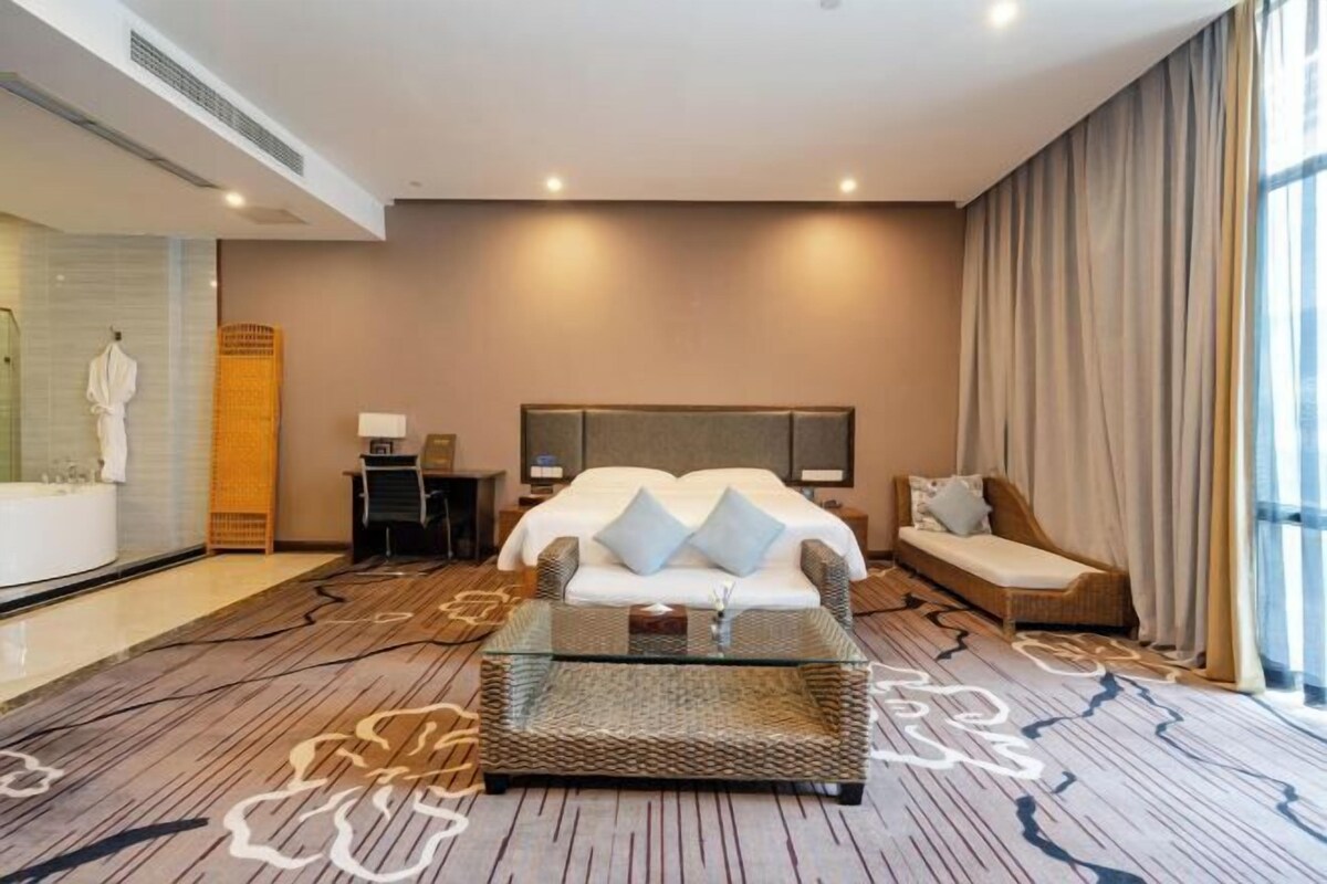 A hotel room with a large bed, a sitting area with a glass coffee table, a small desk, and a bathroom with a bathtub and a shower.