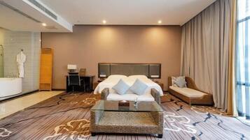 A hotel room with a large bed, a sitting area with a glass coffee table, a small desk, and a bathroom with a bathtub and a shower.