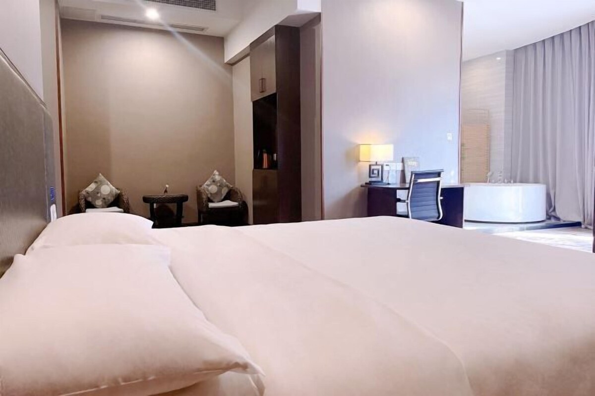 A hotel room with a large bed, a desk with a lamp, a chair, and a bathroom area.
