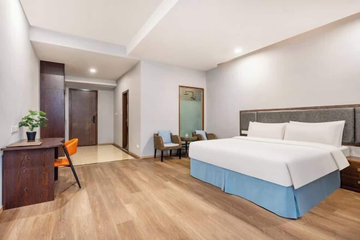 Habitación de hotel con una cama grande, un escritorio con silla, una mesita con sillas y una planta en maceta.