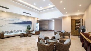 A spacious lobby with a high ceiling, a seating area with wicker chairs and a sofa, a large mural depicting a landscape, and a reception desk with a television. - Manfu Hotel (Beibei Southwest University Zhuangyuanbei Subway Station Branch) (Chongqing)