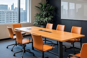 Un salón de conferencias con una mesa larga, seis sillas, una pantalla de proyector y un amplio ventanal con vistas a la ciudad.