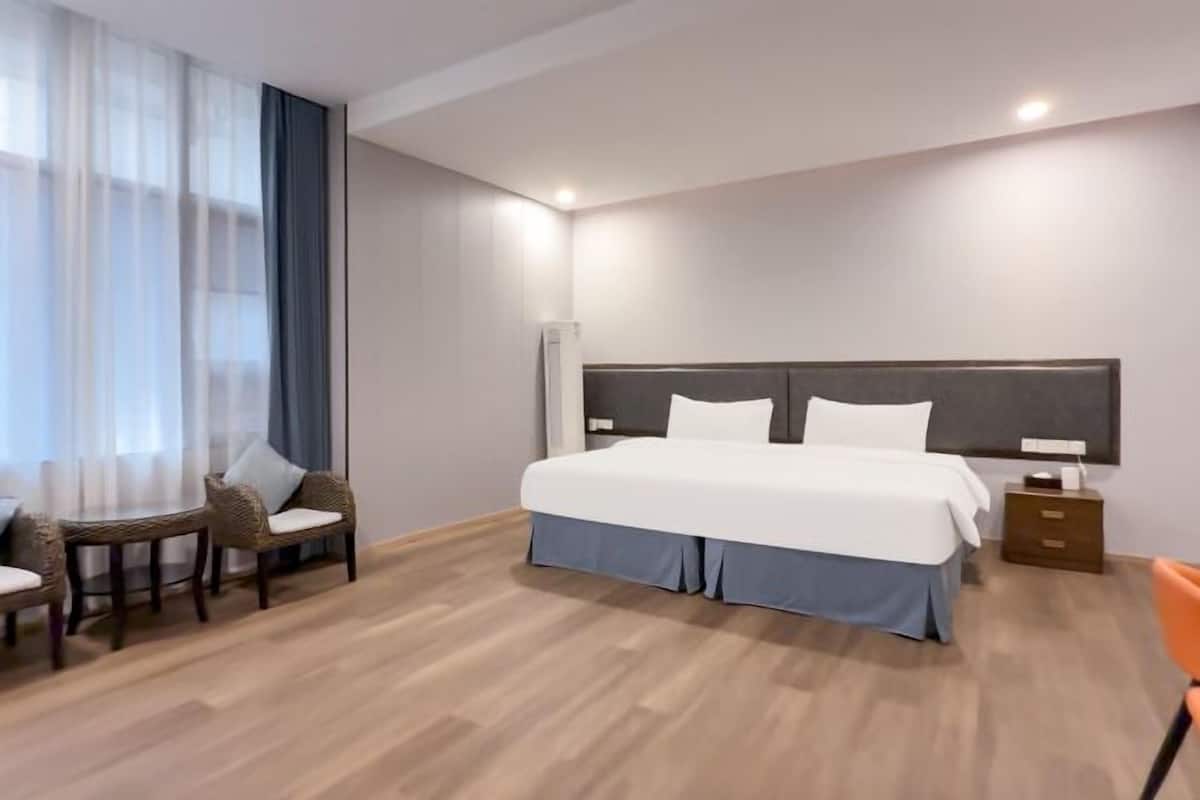 Habitación de hotel con cama, mesita de noche, una silla, una pequeña mesa y una ventana con cortinas.