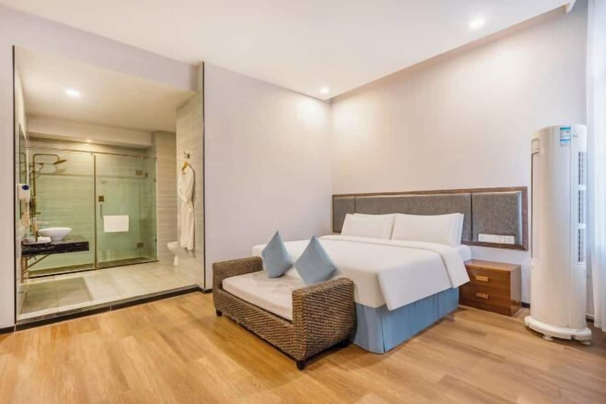 Un dormitorio moderno con cama, una silla de mimbre, una mesita de noche y un área de ducha con mampara de vidrio.