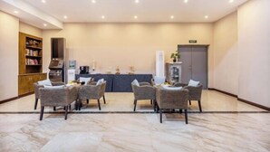 A spacious lobby with a marble floor, a reception desk, a bookshelf, and wicker chairs arranged around a small table. - Manfu Hotel (Beibei Southwest University Zhuangyuanbei Subway Station Branch) (Chongqing)