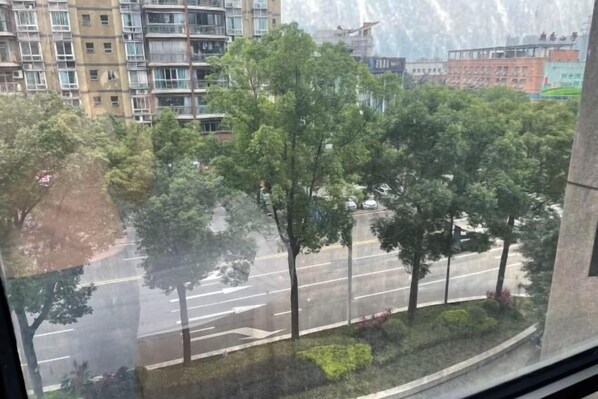 A view of a multi-story residential building with balconies, a street with parked cars, and trees in the foreground. - Manfu Hotel (Beibei Southwest University Zhuangyuanbei Subway Station Branch) (Chongqing)