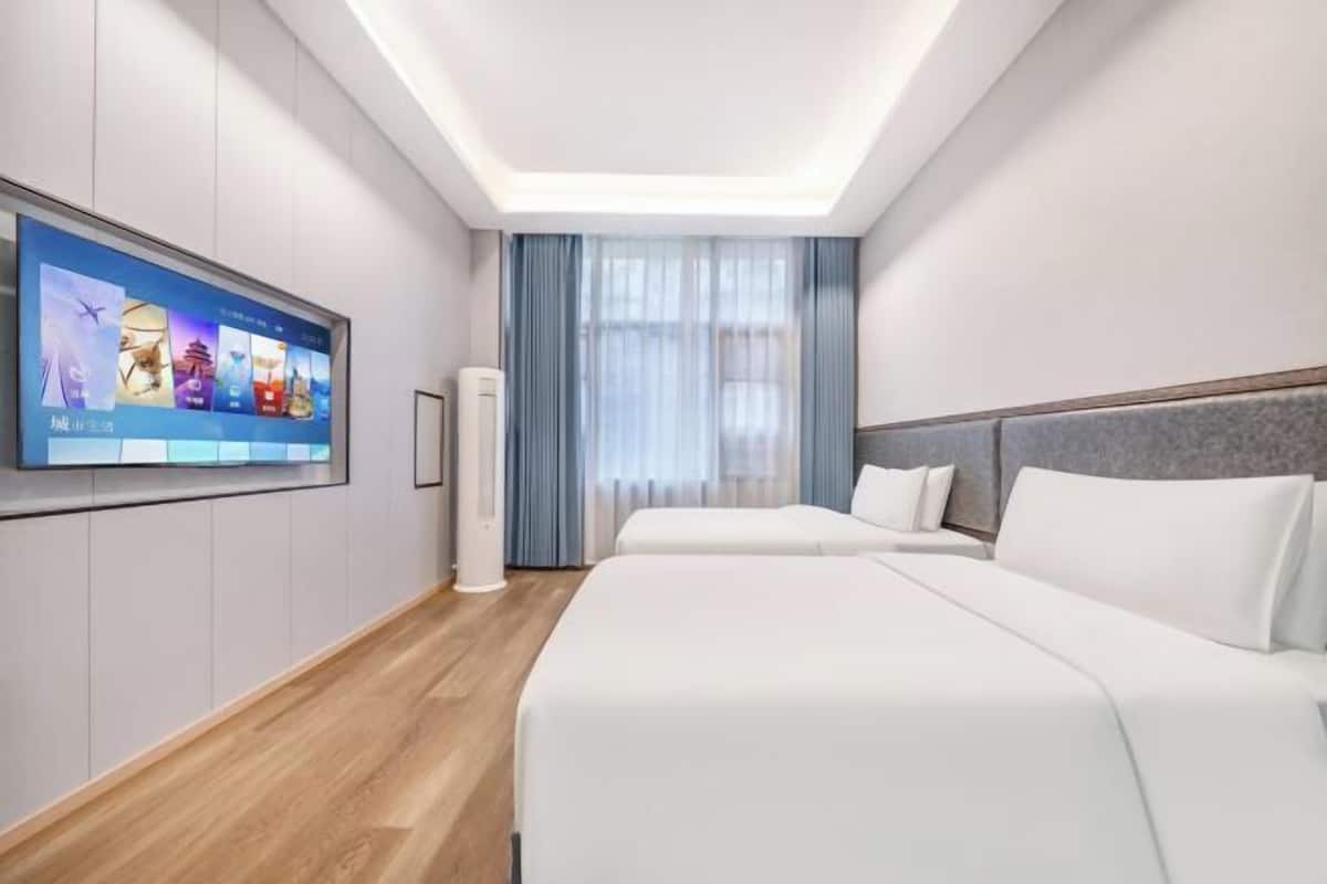 Habitación de hotel moderna con una televisión de pantalla plana grande, una cama, una mesita de noche y una ventana con cortinas.