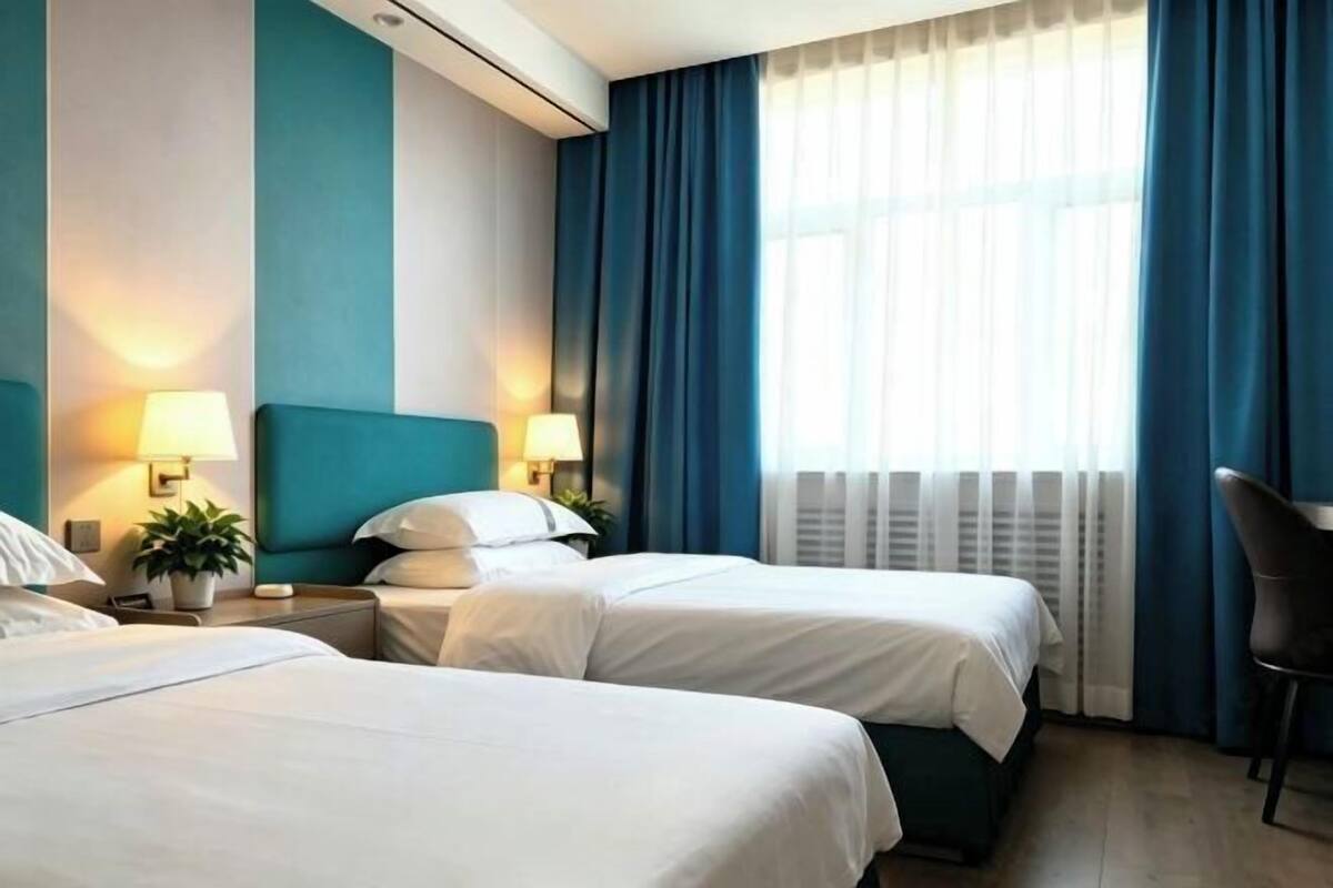 A hotel room with two beds, a desk, a chair, and a large window with curtains.