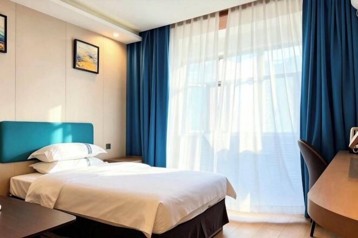 A hotel room with a bed, a desk, a chair, and a window with curtains.