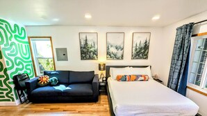 A modern bedroom with a black sofa, a large bed with a white mattress, and three framed nature paintings on the wall.
