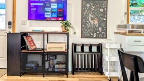 A modern living room with a flat-screen TV displaying a streaming service interface, a decorative wall art piece, and a compact shelving unit with books and a plant.