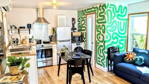 A modern kitchen with stainless steel appliances, a dining area with a table and chairs, and a living room with a sofa and decorative pillows.