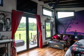 A room with a large sliding glass door, a leather sofa, a bed with a floral bedspread, and a mural of a tree with bats.