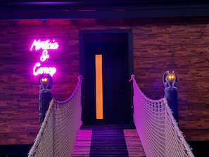 A neon sign reading "Marta & Co" on a wooden wall, leading to a door with a vertical orange stripe. - Morticia & Gomez Treehouse. Hot tub. Riverfront. (Sevierville)