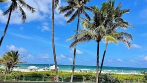 A balcony with lounge chairs overlooking a beach with palm trees and a clear blue sky. - Pretty Oceanfront Condo 2 BR w/direct access Beach (Miami)