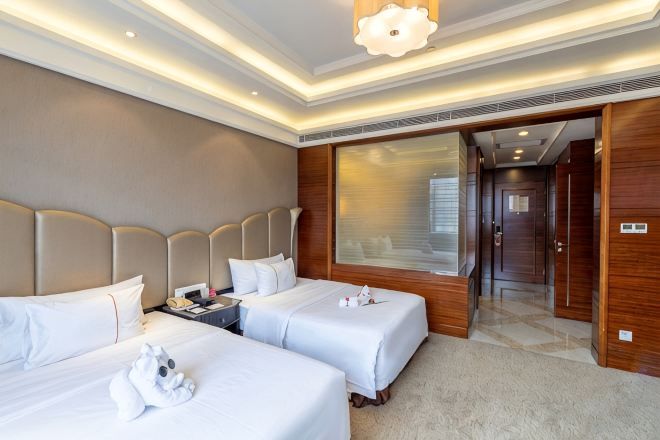 A hotel room with two beds, a large window, and a door leading to a hallway.