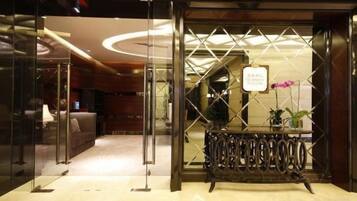 A hotel entrance with a reception desk, glass doors, and a modern interior design.