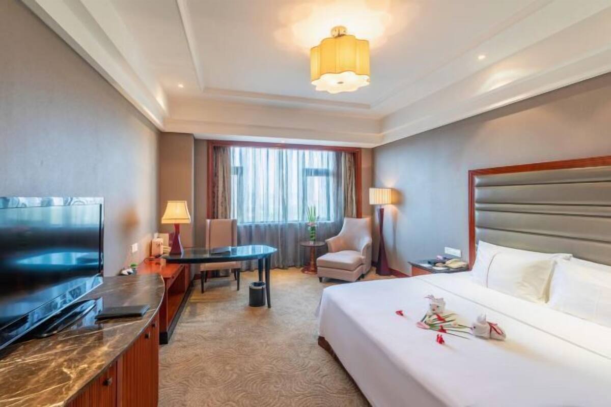 A hotel room with a bed, a desk, a chair, a TV, and a lamp.