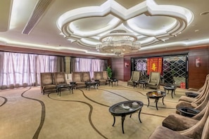 Et hotellobby med en moderne lysekrone, behagelige siddepladser og et stort vindue med gardiner.