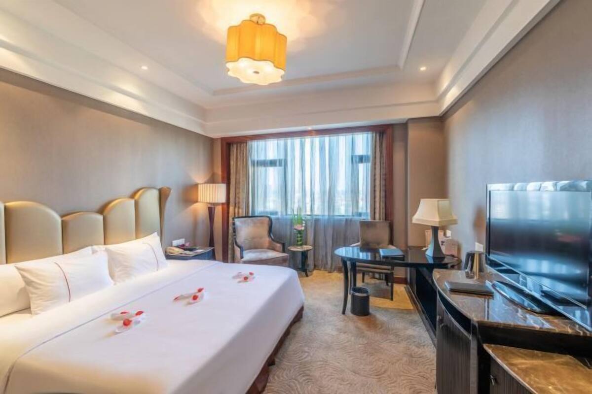 A hotel room with a large bed, a desk with a chair, a television, and a window with curtains.
