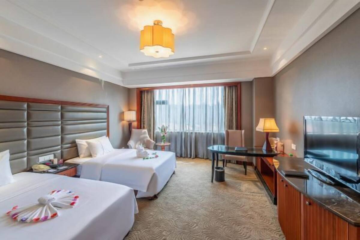 A hotel room with two beds, a TV, a desk, and a window with curtains.