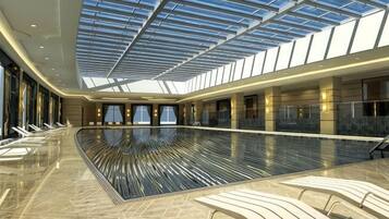 Una piscina interior espaciosa con techo de cristal, rodeada de sillones de descanso.