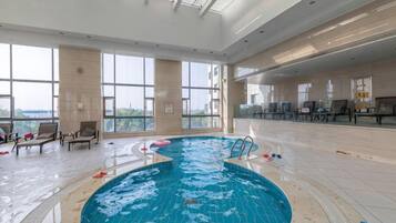 An indoor swimming pool with clear views of the outdoors, surrounded by lounge chairs and a spacious area.