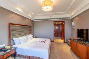 A hotel room with a large bed, a TV, a desk, and a bathroom visible through an open door. - Rich Global Hotel (Li County)