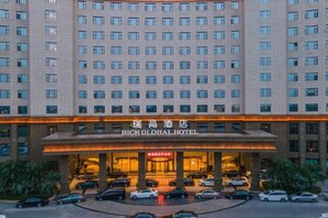 Un hotel con gran número de ventanas, una entrada destacada con un cartel, y varios coches aparcados en la parte delantera.