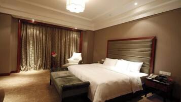 A hotel room with a large bed, a bench, a nightstand, and a curtain-covered window.