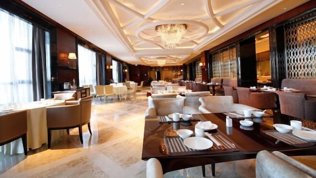 A spacious hotel dining area with multiple tables and chairs, a large chandelier, and large windows providing natural light. - Rich Global Hotel (Li County)