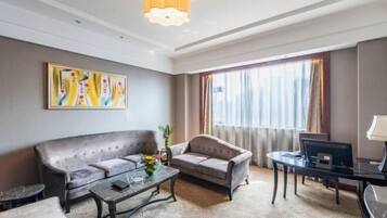 Ein modernes Hotelzimmer mit Sofa, Sessel, Couchtisch und Schreibtisch mit Computer.