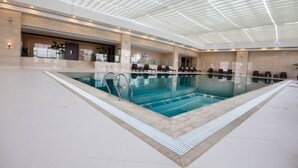Una amplia piscina cubierta con diseño moderno, rodeada de sillones de descanso y una zona techada con estructura en el techo.